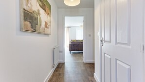 A hallway with a radiator, a painting, a door, and a view into a room with a bed and curtains.