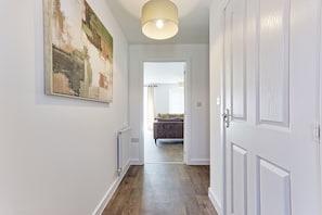 Un couloir avec un radiateur, un tableau, une porte et une vue sur une pièce où se trouvent un lit et des rideaux.