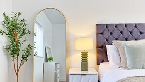 A bedroom with a bed, a nightstand with a lamp, a mirror, and a potted plant.