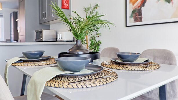 A modern dining area with a white table, grey cabinets, a microwave, and a potted plant.