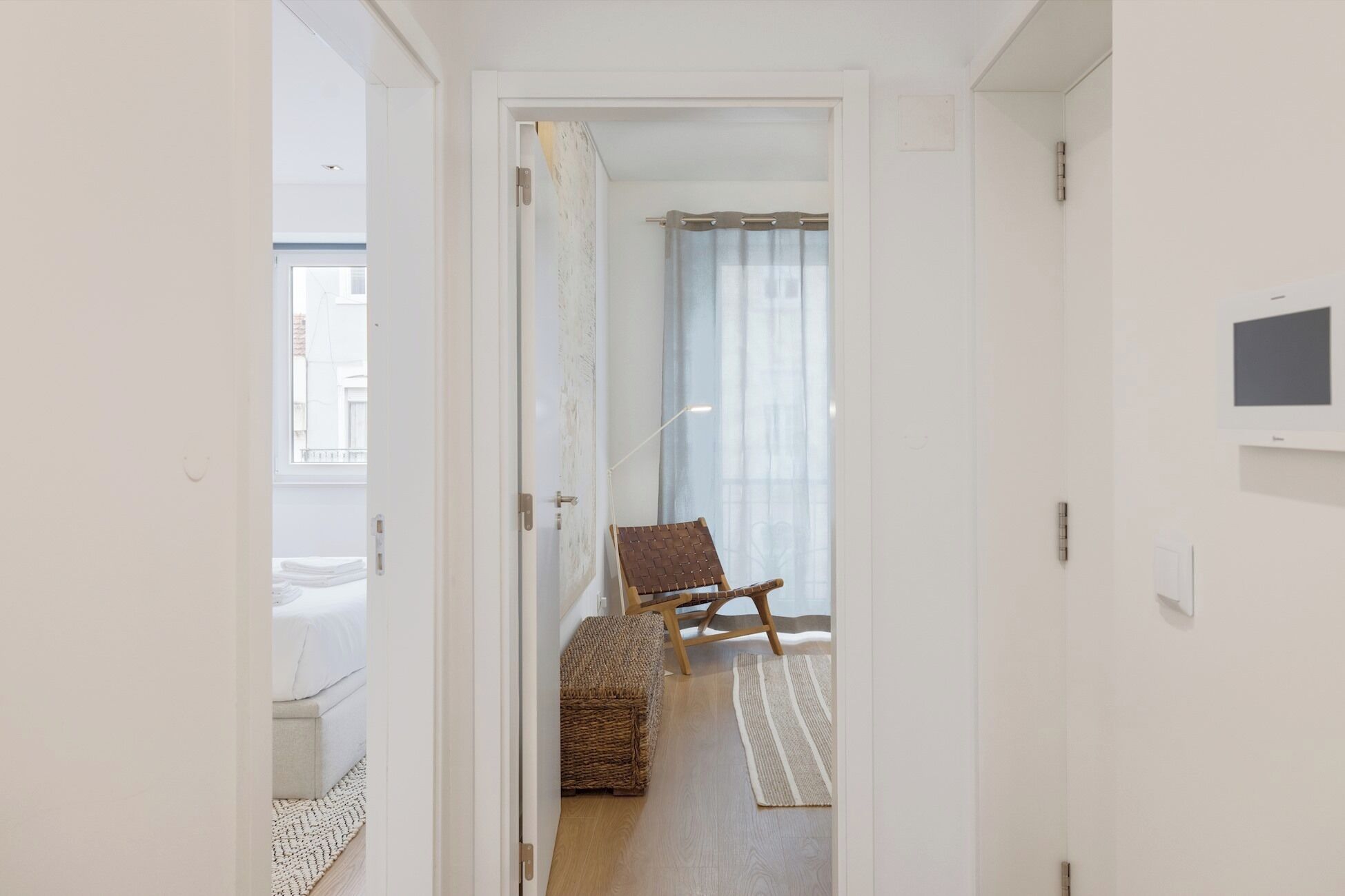 A hallway leading to a bedroom with a bed, a chair, a woven basket, and a TV on the wall.