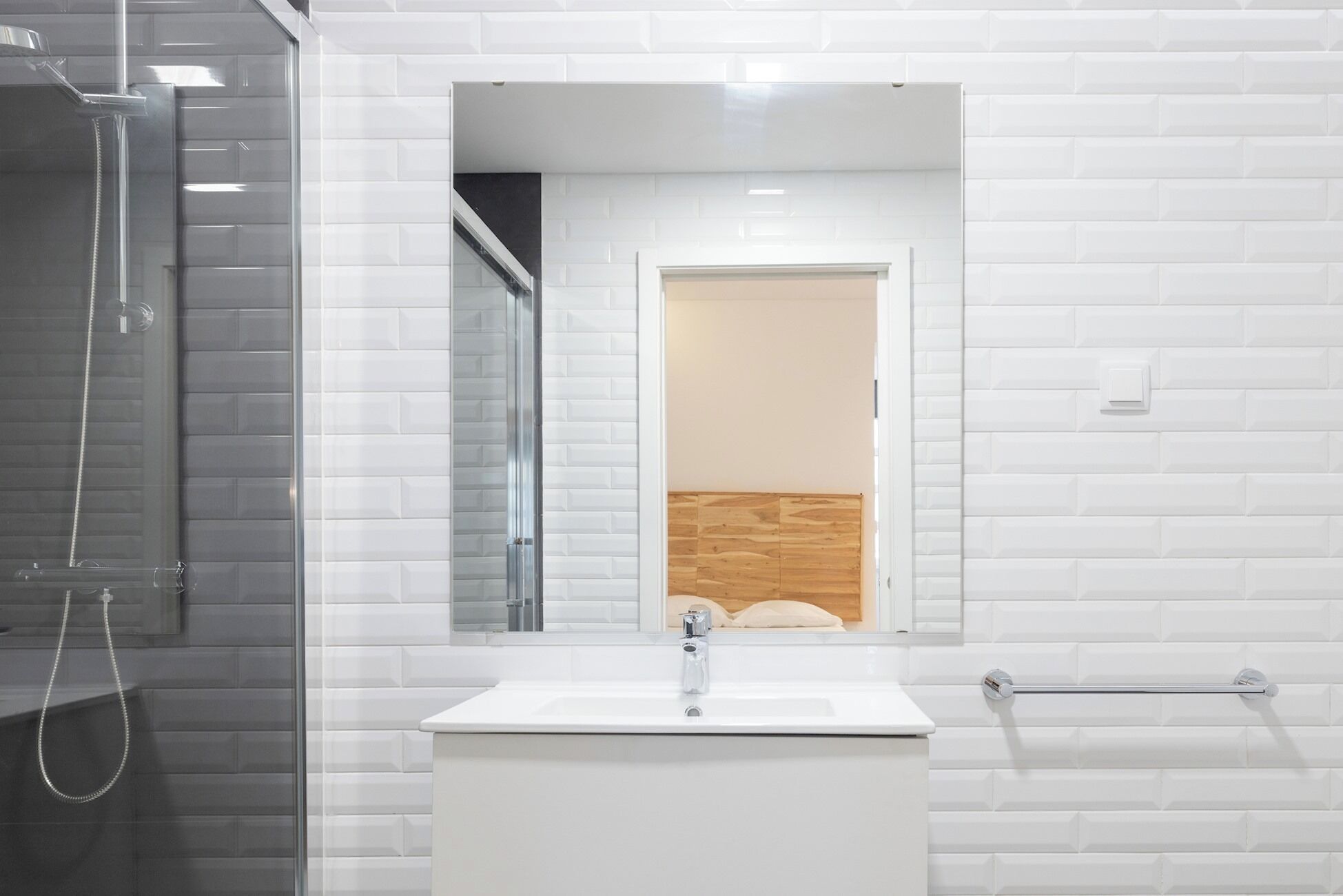 Une salle de bain avec un mur recouvert de carreaux blancs, une douche en verre, un lavabo blanc et un mur recouvert de panneaux en bois.