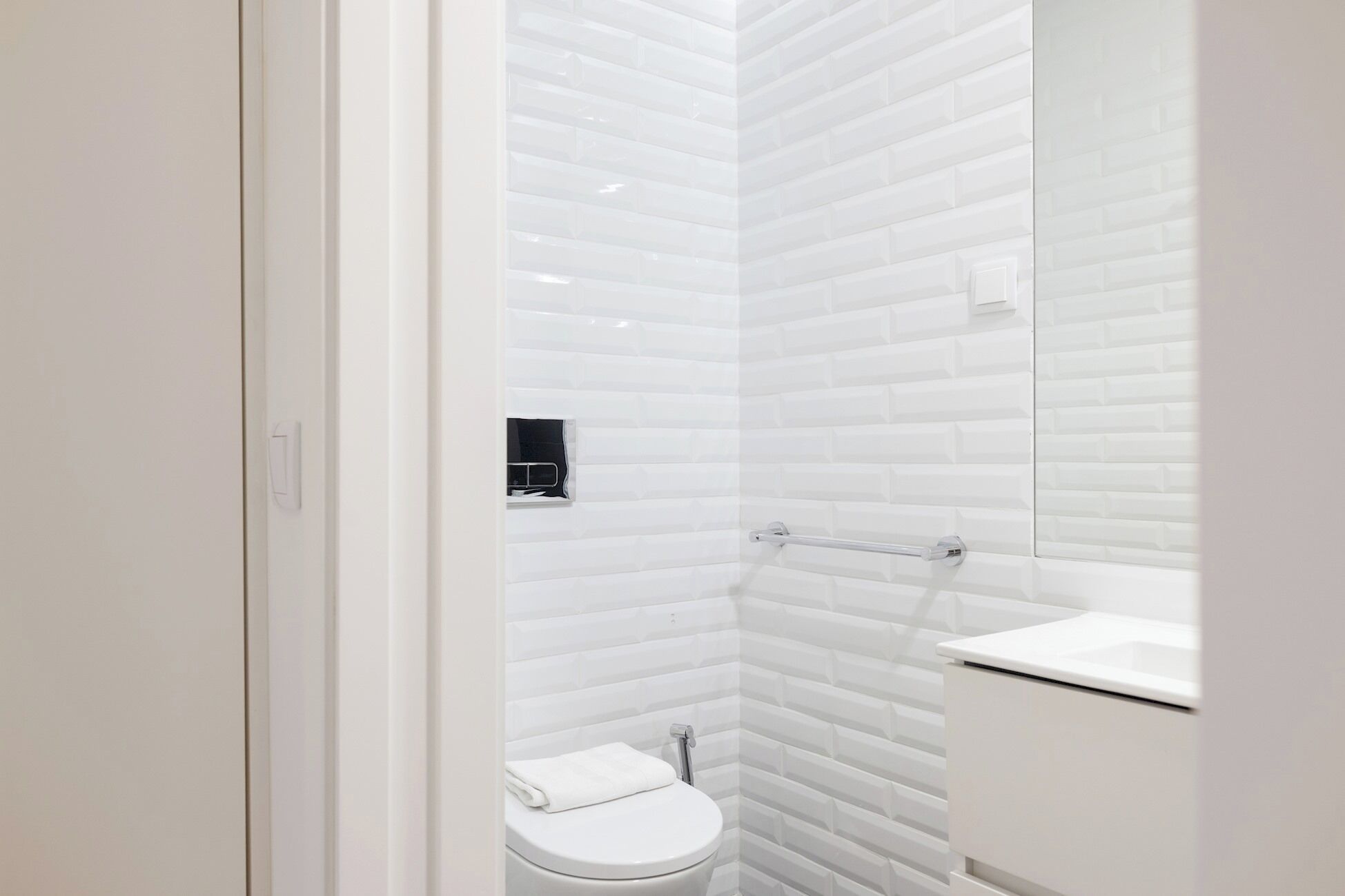 A bathroom with white tiled walls, a toilet, a towel rack, and a mirror.