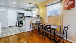A modern kitchen with white cabinets, a dining area with a wooden table and chairs, and a window with curtains. - 3BR Near Takoma Metro & DC Hospitals (Washington)