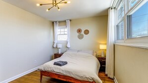 A bedroom with a wooden bed, a window with curtains, a bedside lamp, and a wall-mounted light fixture. - 3BR Near Takoma Metro & DC Hospitals (Washington)