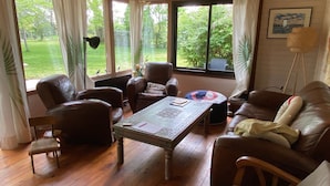 Una stanza accogliente con pavimento in legno, mobili in pelle, un tavolo con tovaglia decorativa e ampie finestre con tende.
