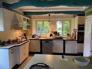 Una cocina equipada con lavavajillas, estufa y diversos electrodomésticos. Se aprecia una ventana con vistas a zonas verdes.