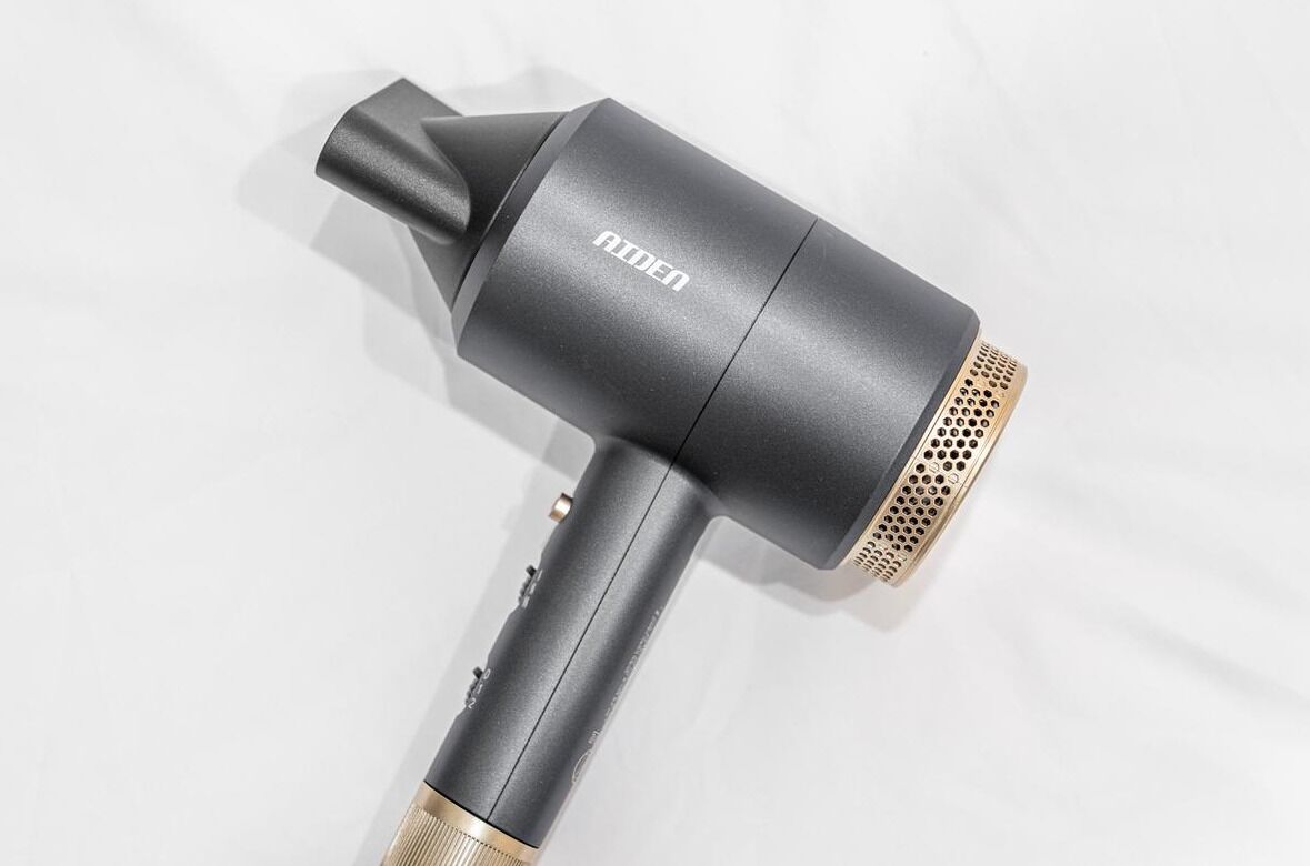 A hair dryer with a black handle and a gold nozzle, placed on a white surface.