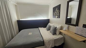 A bedroom with a bed, a bedside table, a mirror, a wall art piece, and a window with curtains.
