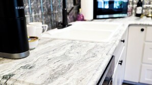 A kitchen with a marble countertop, a coffee maker, a clock, and a television. - Saint Jo Wine Country Loft Near Blue Ostrich Winery (Saint Jo)