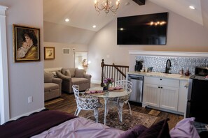 A cozy living area with a sofa, a dining table with chairs, a kitchen with a tiled backsplash, and a staircase.