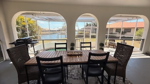 A covered patio with a wooden table and chairs, overlooking a pool and a residential area. - Waterfront home with pool, billiards, 4 min beach (Punta Gorda)