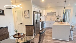 A modern kitchen with white cabinets, a central island, and a dining area with wicker chairs and a glass table. - Waterfront home with pool, billiards, 4 min beach (Punta Gorda)