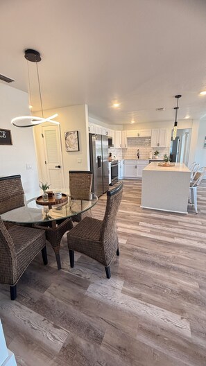 A modern kitchen with white cabinets, a central island, and a dining area with wicker chairs and a glass table. - Waterfront home with pool, billiards, 4 min beach (Punta Gorda)