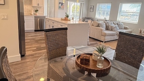 A modern living room with wicker furniture, a glass coffee table, and a kitchen in the background. - Waterfront home with pool, billiards, 4 min beach (Punta Gorda)
