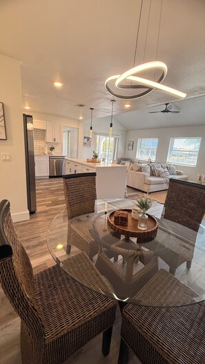 A modern living room with wicker furniture, a glass coffee table, and a kitchen in the background. - Waterfront home with pool, billiards, 4 min beach (Punta Gorda)