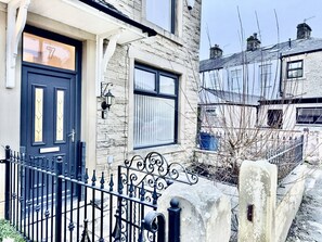 Une maison en pierre avec une porte bleu foncé, une clôture en métal noir et un mur en pierre.