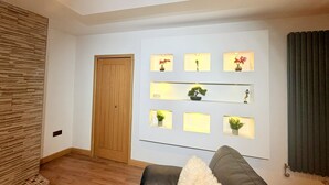 Een woonkamer met een houten deur, een bank en wandplanken met planten.