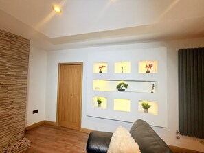 Un salon avec une porte en bois, un canapé et des étagères murales ornées de plantes.