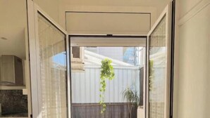 Ein Zimmer mit einer Schiebetür zu einer Terrasse im Freien, die einen Holzboden, eine hängende Pflanze und einen Blumentopf hat.