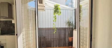 A room with a sliding glass door leading to an outdoor patio with a wooden deck, a hanging plant, and a potted plant.