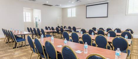 A conference room with multiple tables and chairs, equipped with water bottles and a projector screen.