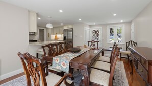 Comedor con una larga mesa, sillas de madera y un mantel con estampado floral.