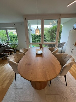 Ein moderner Essbereich mit einem Holztisch, sechs Stühlen und großen Fenstern mit Blick auf Grünflächen.