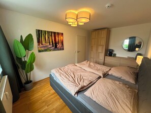 Ein Schlafzimmer mit einem Bett, einer großen Topfpflanze, einem Gemälde, einem Kleiderschrank, einem Spiegel und einer Deckenleuchte.