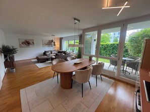 A modern living room with a dining area, large windows, and a view of greenery. - Feel-good oasis in Augsburg's architectural jewel! (Augsburg)