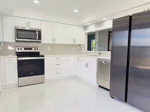 A modern kitchen with white cabinetry, a stainless steel refrigerator, a microwave, and a dishwasher. - La B Villa (Cape Coral)