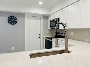 Una cocina moderna con armarios blancos, un lavamanos de acero inoxidable, un microondas y un reloj en la pared.