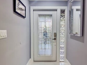 Una puerta con un diseño geométrico de vitral, un letrero enmarcado en la pared, y un espejo que refleja la puerta.