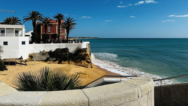 Hotel a la costa amb vistes al mar, palmeres i un edifici blanc amb teulada vermella.