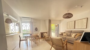 Àmplia zona d'estar amb sofà, cadires, taula de dinar i zona de cuina amb finestra.