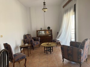 Ein Wohnzimmer mit einem Holzkabinett, zwei Sesseln, einem kleinen runden Tisch und einer Deckenleuchte.
