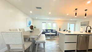A modern kitchen with a central island, dining area with a bench, and a living room with a sofa and coffee table. - Casa Azul/Tropical Paradise/Heated Pool/Private (Cape Coral)