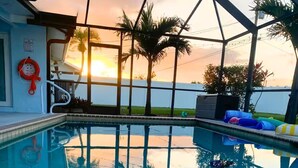 A swimming pool with a glass ceiling, palm trees, and a sunset view. - Casa Azul/Tropical Paradise/Heated Pool/Private (Cape Coral)