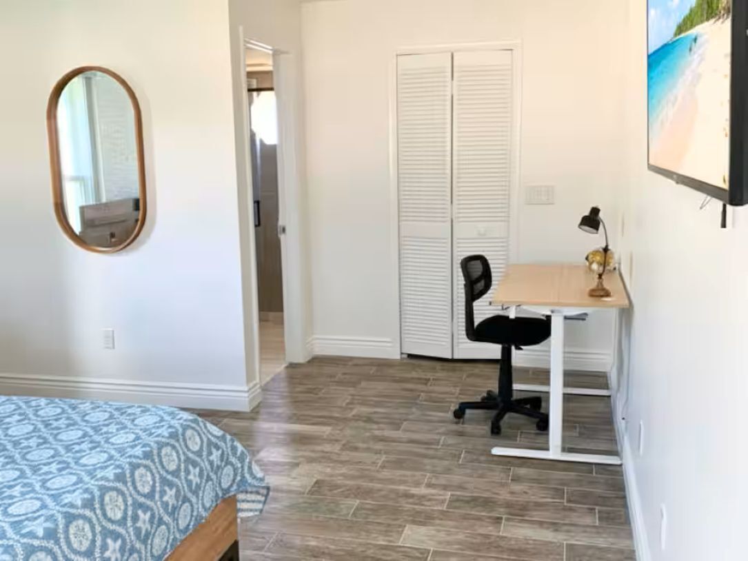 A bedroom with a bed, a desk with a chair, a mirror, and a closet.