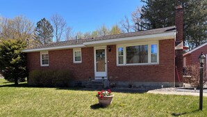 A single-story brick house with a front porch, a potted plant, and a clear blue sky. - Beautiful, Family friendly home in Saratoga Springs, NY. 2.2 Miles from track, (Saratoga Springs)