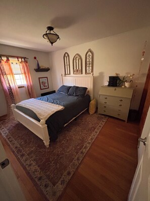 A bedroom with a bed, a dresser, a window with curtains, and a ceiling fan.