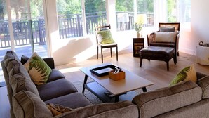 Ein geräumiger Wohnbereich mit Deckenventilator, großen Fenstern, einer Couch, einem Couchtisch und einem Sessel.