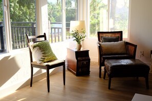 A room with a wooden floor, a chair with a green pillow, a sofa with a brown cushion, a lamp, and a bookshelf.