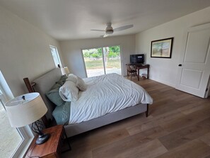 A bedroom with a bed, a desk, a chair, a ceiling fan, and a door.