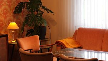 A dining area with a table, chairs, a potted plant, a lamp, and a sofa.