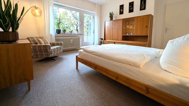 A bedroom with a bed, a wooden wardrobe, a chair, a desk, and a radiator. - "Anno 1973" - Start your journey through time today! PRIMA Quarter (Lastrup)