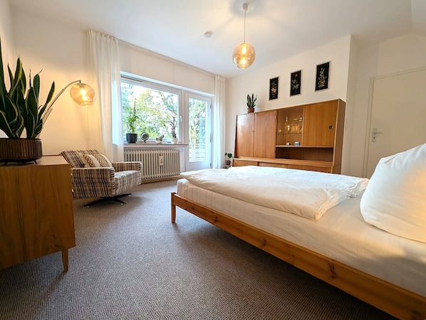 Ein Schlafzimmer mit einem Bett, einem Holzschrank, einem Stuhl, einem Schreibtisch und einer Heizung.