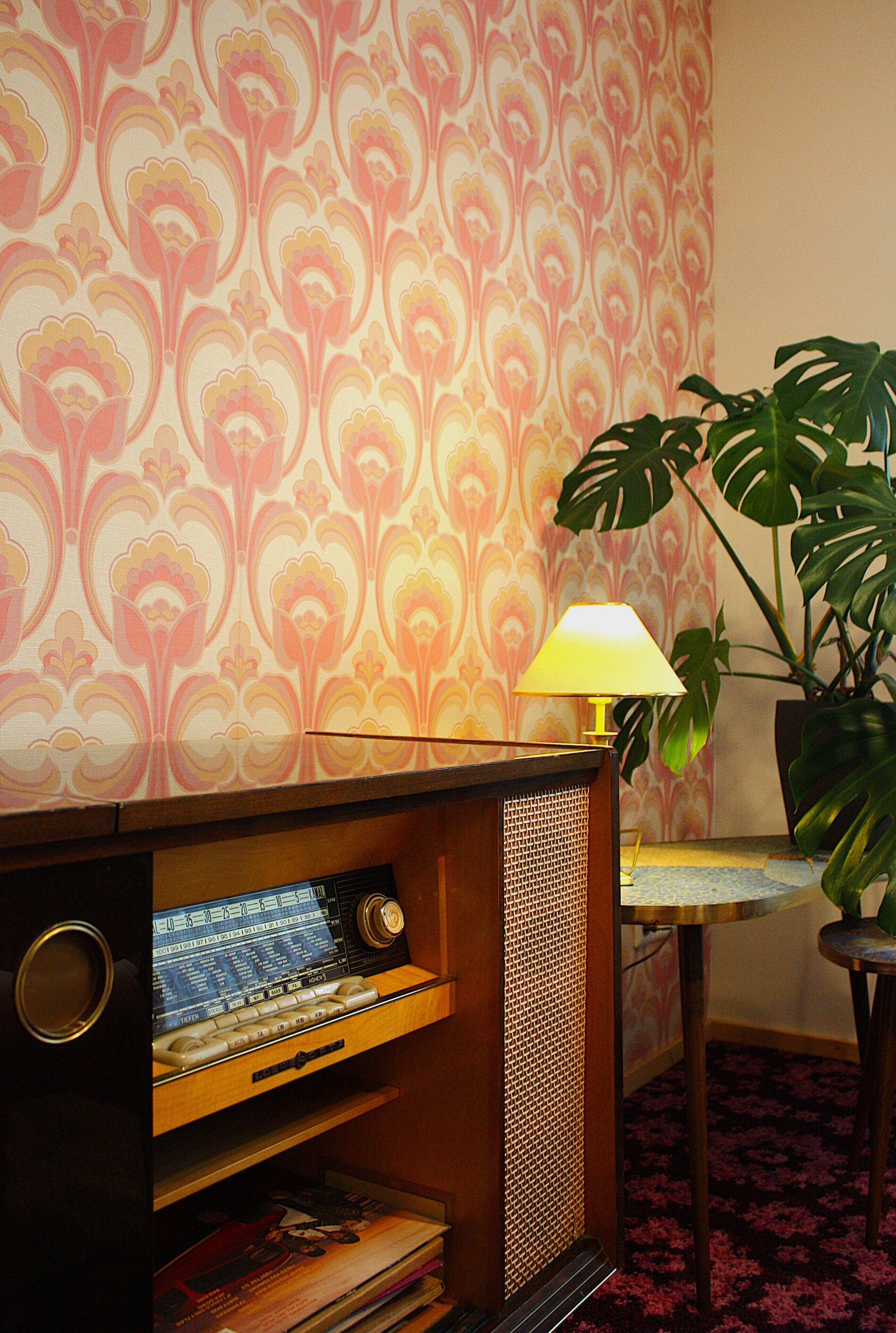 Et værelse med tapet, en radio, en lampe og en potteplante.