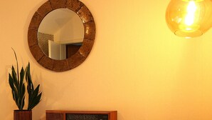 A living room with a patterned armchair, a wooden cabinet, a radio, a round mirror, and a hanging light fixture. - "Anno 1973" - Start your journey through time today! PRIMA Quarter (Lastrup)