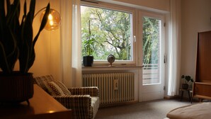 A room with a large window, a radiator, a chair, a bedside table, and a bedside lamp. - "Anno 1973" - Start your journey through time today! PRIMA Quarter (Lastrup)